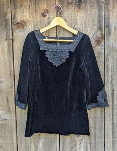 Beautiful black velvet crochet tunic top, 1970s vintage A lovely romantic bohemian piece.... Features a lush black velvet, flattering square neckline with woven 'lace' detailing, bell bracelet sleeves with matching lace, a loose boxy fit, just-over-the-hips hemline, and lots of whimsical Gothic glamour... Would look perfect Wednesday Addams style with white tights and Mary Janes, or given a modern edge with skinny jeans and ankle boots...;) Brand : Butte Knit No size  labeled, I'd say fits like a Medium Fabric has a little stretch to it, allowing some leeway All measurements taken with garment lying flat, double where necessary 14.5 inches shoulder seam to shoulder seam 17 inches pit to pit 21 inches across hem 25 inches from neckline to hem 15 inch sleeve length Some minor general fabric Whimsigoth Tops, Whimsical Gothic, Bell Bracelet, Bell Sleeves Top, Velvet Crochet, Bohemian Goth, Gothic Glamour, Black Bell Sleeve Top, Crochet Neckline