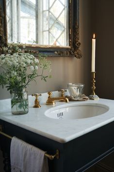 a white sink sitting under a mirror next to a vase with flowers on top of it