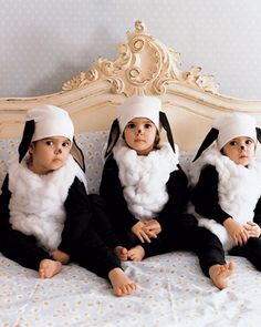 three babies dressed in costumes sitting on a bed with their heads turned to look like rabbits