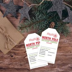 two north pole delivery tags sitting on top of a wooden table next to a christmas tree