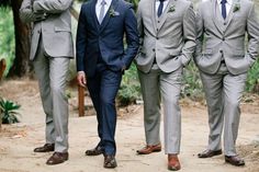 four men in suits standing next to each other on a dirt path with trees in the background