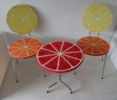 three oranges and one grapefruit are sitting on small metal tables with legs