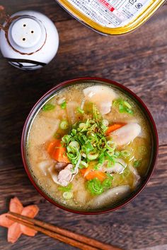 a bowl of soup with carrots, celery and meat in it on a wooden table