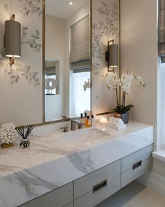 a bathroom sink with two mirrors above it and flowers in the vase on the counter