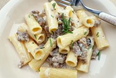 a white plate topped with pasta covered in meat and sauce next to a silver fork