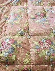 a pink and blue flowered comforter is laying on a bed with a pillow