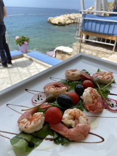 shrimp and olive appetizer served on a white platter overlooking the water's edge