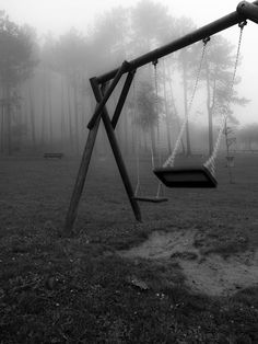 an empty swing set in the middle of a foggy park