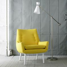 a yellow chair sitting next to a lamp on top of a wooden floor in front of a gray wall