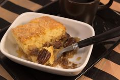 a piece of cake in a white dish with a fork and coffee mug on the side