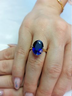 a woman's hand with a blue ring on top of her finger and the other hand holding an engagement ring