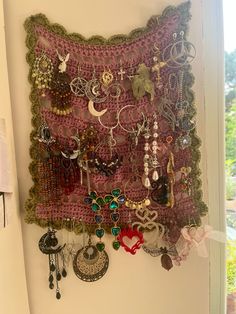 there is a wall hanging with many different pieces of jewelry on it and a window in the background