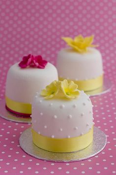 three small cakes with yellow and pink flowers on them are sitting on a polka dot tablecloth