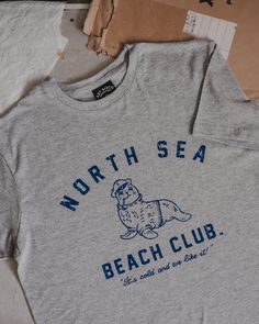 Our North Sea Beach Club t-shirt with its hand-drawn print celebrates our appreciation of our mighty coastline. The cold doesn't stop the wild spirited from swimming, paddle boarding and surfing its crashing waves. There is a certain pride and camaraderie when plunging into its bracing blue waters. It's cold and we like it! * Unisex relaxed fit * Crew neck * Distressed print on front * 50% cotton / 50% polyester * Machine wash at 30o / Do not tumble dry / Iron on reverse  Each of our classic super soft grey tees are screen printed in Yorkshire using blue ink, the design is distressed to give a vintage look. Graphic Print Top For Beach Season, Outdoor Graphic Print Crew T-shirt, Graphic Print Crew T-shirt For Outdoor, Outdoor Crew Neck T-shirt With Graphic Print, Outdoor Crew T-shirt With Graphic Print, Graphic Print Crew Top For Surfing, Bracing Blue, Mermaid Sweatshirt, Art Disco