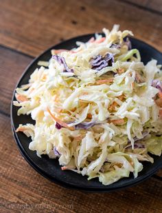 a black plate topped with coleslaw slaw on top of a wooden table