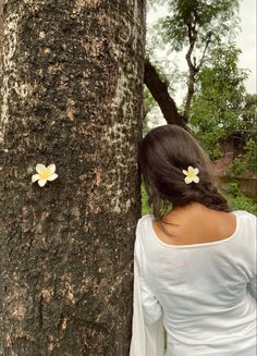 a woman standing next to a tree with two flowers on it's back end