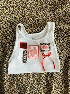 a white tank top with an animal print design on the front and red ribbon at the bottom