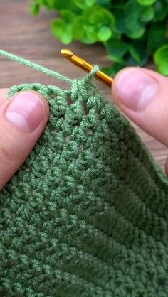 a person holding a crochet hook in front of a green piece of cloth