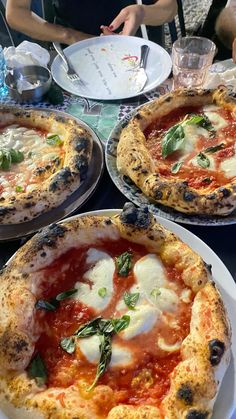 three pizzas with sauce, cheese and spinach on plates at a restaurant table