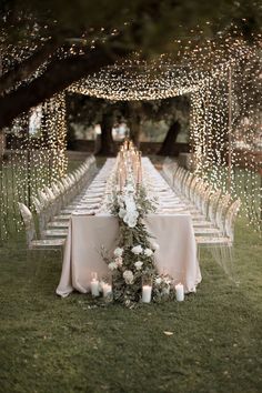 a long table with white flowers and candles on it in the middle of a field