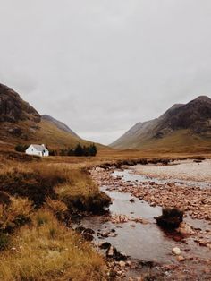 a small white house sitting on top of a lush green hillside next to a river