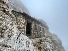 an old stone building on the side of a mountain with a window in it's wall