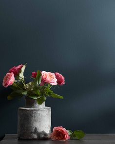 some pink roses are in a gray vase on a wooden table next to a blue wall