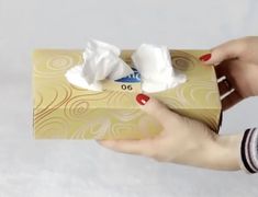 a hand holding a box with cotton in it and two small pieces of tissue on top