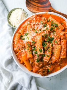 a white bowl filled with pasta and sauce next to a wooden spoon on top of a towel