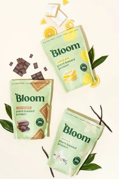 three bags of bloom tea sitting on top of a white table next to some leaves