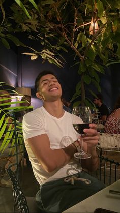 a man sitting at a table with a glass of wine in his hand and smiling