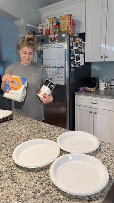 a woman standing in a kitchen with three plates on the counter and one holding a carton of milk