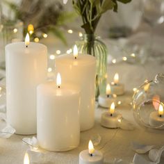 three white candles sitting on top of a table next to flowers and glass vases