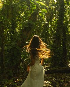 a woman in a white dress is walking through the woods with her hair blowing in the wind