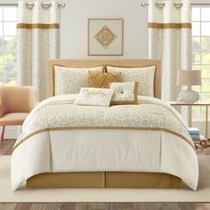 a bed with white and gold comforters in a bedroom next to a window filled with curtains