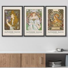 three framed art prints on the wall above a cabinet in a room with bookshelves