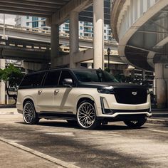 a white and black suv parked in front of an overpass with buildings in the background