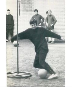 an old black and white photo of a young man kicking a soccer ball on the ground