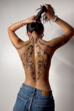 the back of a woman with tattoos on her body and hands behind her head, standing in front of a white wall