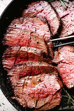 steaks in a skillet with tongs on the side and rosemary sprigs