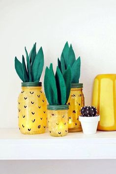 three pineapple painted mason jars sitting on a shelf next to a potted plant