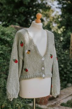 a white mannequin wearing a green cardigan with red flowers and bees on it