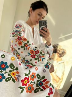 a woman is taking a selfie with her cell phone while wearing an embroidered dress