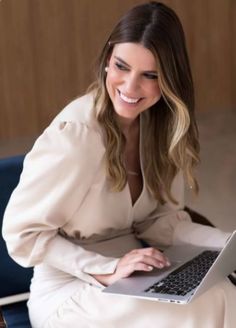 a woman sitting on a chair with a laptop in her lap and smiling at the camera