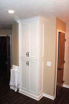 a white cabinet in the corner of a room next to a door and towel rack