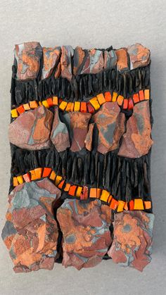 a piece of art made out of rocks with orange and black beads on it's sides