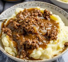 a white bowl filled with mashed potatoes covered in gravy and meat sauce