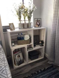 a white shelf with baskets and flowers on top in a room next to a window