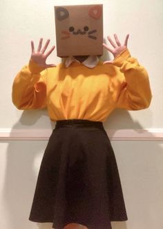 a person with a box on their head and hands in front of them, standing against a wall