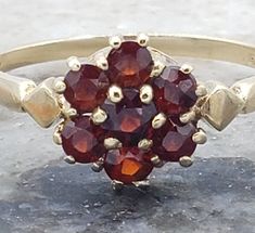 This vintage ring has me believing in the flowers of spring. The juicy red garnets sparkle and shine in this lovely ring.  The history of garnet dates back to the Bronze Age, more than 5000 years ago. Its name, which has been used since these ancient times, was derived from the Latin word granatium, which means pomegranate (because the small, red crystals were thought to resemble pomegranate seeds). Garnet has been believed to be extremely beneficial in the realm of business as well. The stone c Vintage Oval Garnet Birthstone Ring, Vintage Garnet Birthstone Rings, Vintage Garnet Birthstone Ring In Yellow Gold, Vintage Gold Garnet Birthstone Ring, Vintage Yellow Gold Garnet Birthstone Ring, Vintage Red Garnet Cluster Ring, Vintage Birthstone Cluster Ring, Vintage Garnet Promise Ring, Vintage Garnet Cluster Ring As Gift